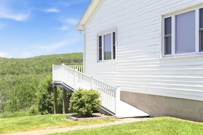 A white house with a wooden deck and a small staircase leading to a porch.