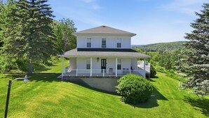 Une maison à deux étages avec un porche, entourée d’une pelouse bien entretenue et d’arbres.