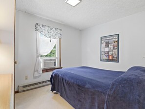 A bedroom with a bed, a window with a curtain, a poster on the wall, and a radiator.