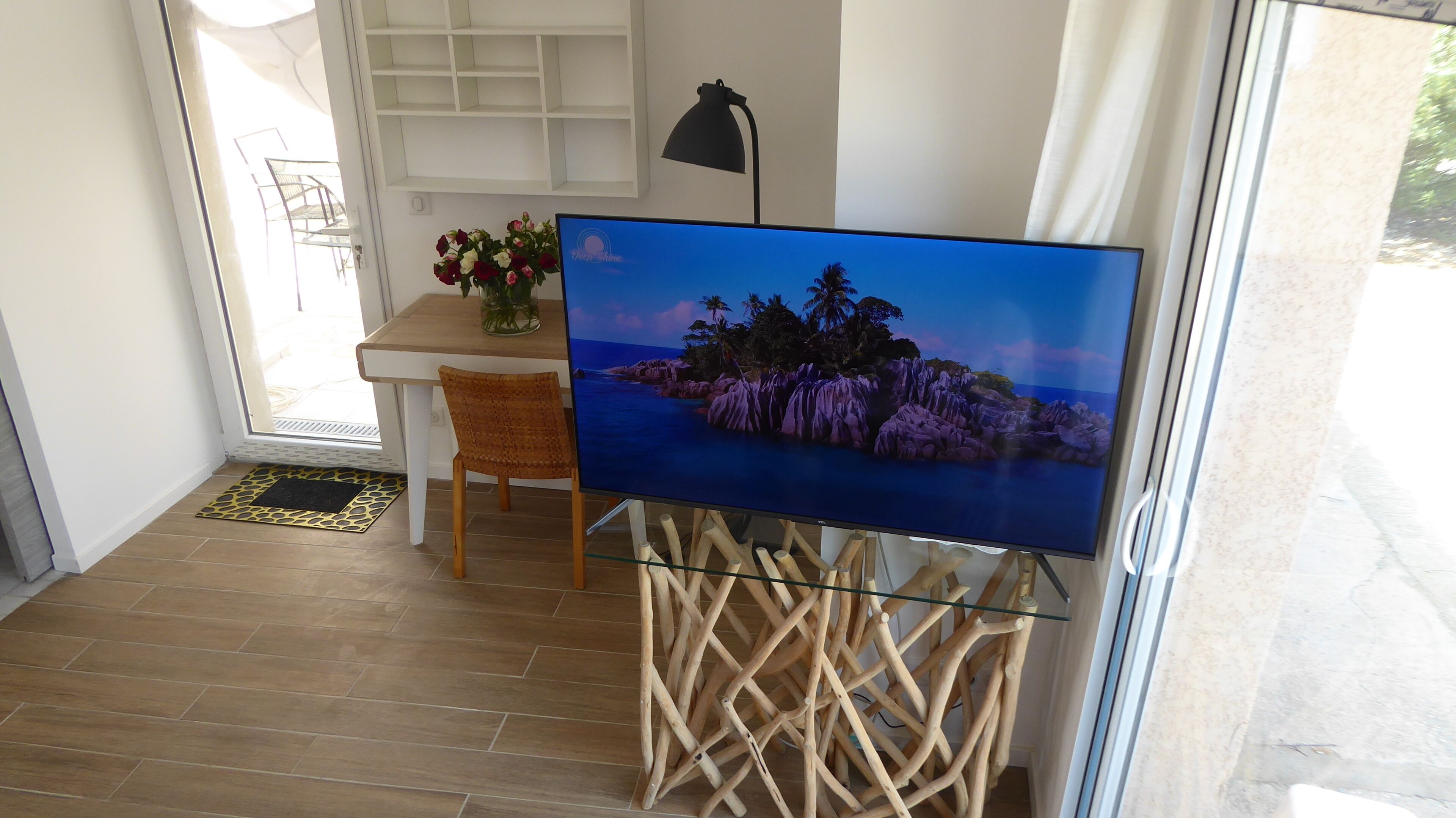 Ein Zimmer mit Fernseher auf einem Glastisch, einem Esstisch mit Stühlen, einer Lampe und einer zur Außenseite führenden Tür.