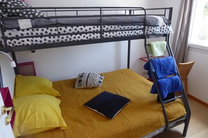 Ein Stockbett mit Kissen und Bettwäsche in Punkten und geometrischen Mustern, eine gelbe Decke und ein blaues Handtuch auf einer Leiter.