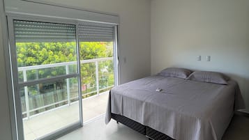 Quarto com uma cama, porta de correr de vidro que dá para uma varanda e luminária no teto.
