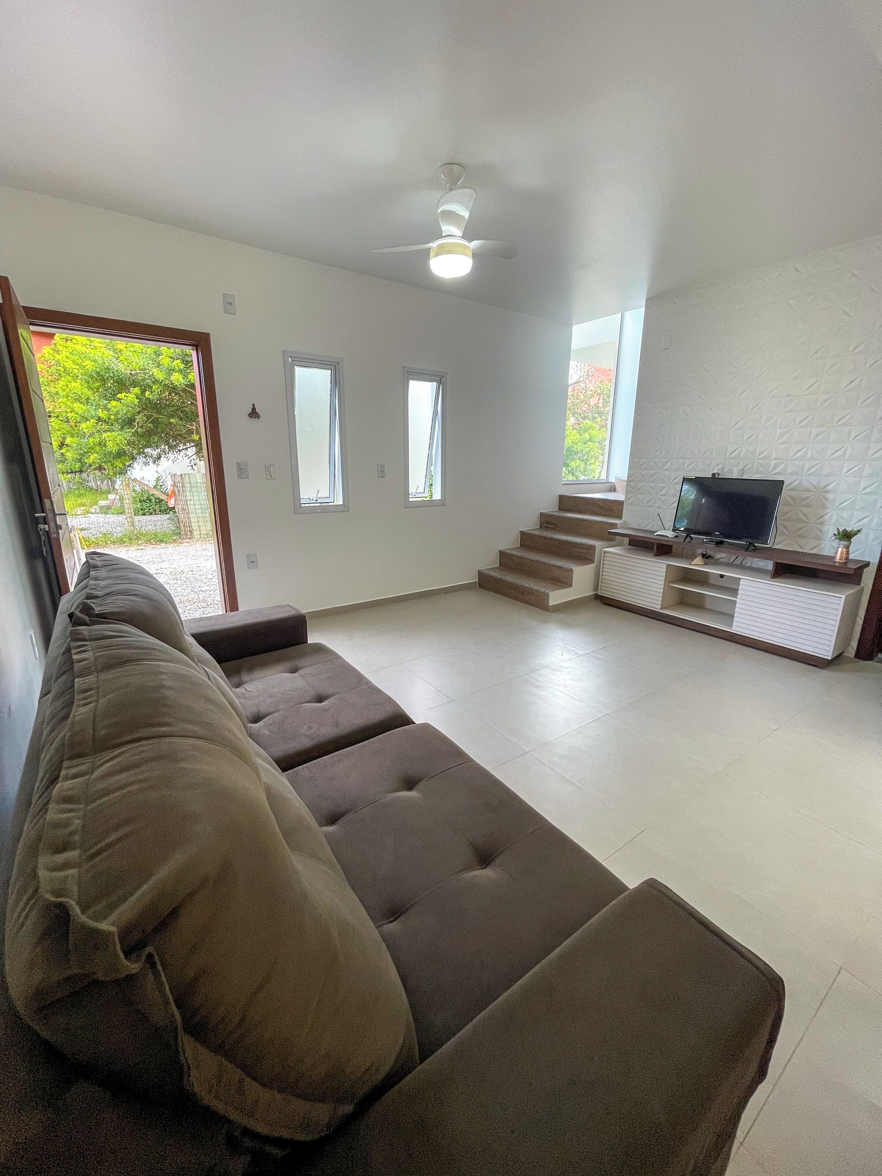 Una sala de estar moderna con un sofá, un televisor sobre un mueble bajo y una escalera que sube a otro nivel.