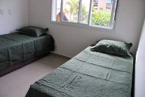 A bedroom with two single beds, a window with a view of greenery, and a white wall. - Azure Riviera Ferrugem (Garopaba)