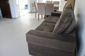 Sala de estar con sofá, una mesa de comedor con sillas y una cocina al fondo.
