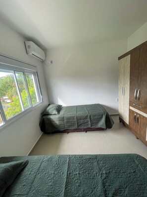 A small, single-bed room with a window, a wardrobe, and an air conditioning unit. - Azure Riviera Ferrugem (Garopaba)