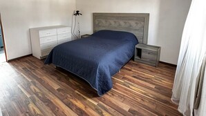 Um quarto com cama, mesa de cabeceira, cômoda e luminária no teto.