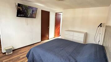 Une chambre à coucher avec un lit, un téléviseur fixé au mur, un plancher en bois et une commode blanche.