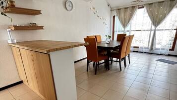 Un coin repas avec une table et des chaises en bois, une horloge au mur et un luminaire suspendu au plafond.