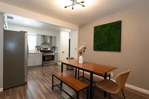 A modern kitchen with stainless steel appliances, a dining area with a wooden table and bench, and a green abstract painting on the wall. - Austin Home with Private Pool & Spa (Austin)