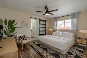 A bedroom with a bed, bedside tables, a ceiling fan, a window with curtains, a door, and a plant. - Austin Home with Private Pool & Spa (Austin)