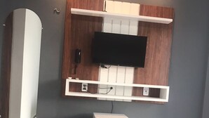 Quarto de hotel com cama, televisão de tela plana presa em um armário de madeira, um refrigerador branco pequeno e um espelho na parede.