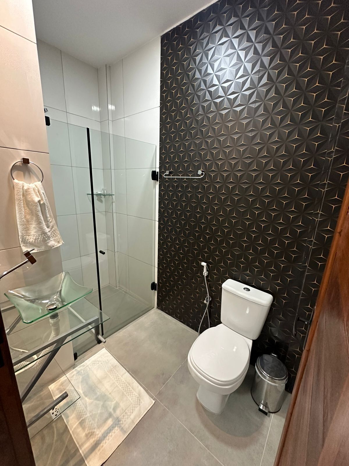 Um banheiro moderno com box de vidro, vaso sanitário branco e parede estampada.