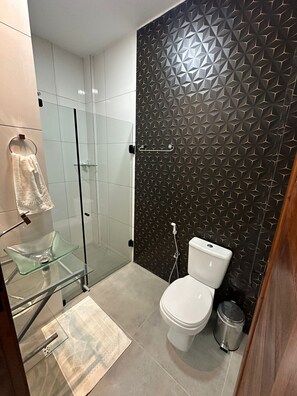 Un baño moderno con cabina de ducha de vidrio, inodoro blanco y pared con estampado.