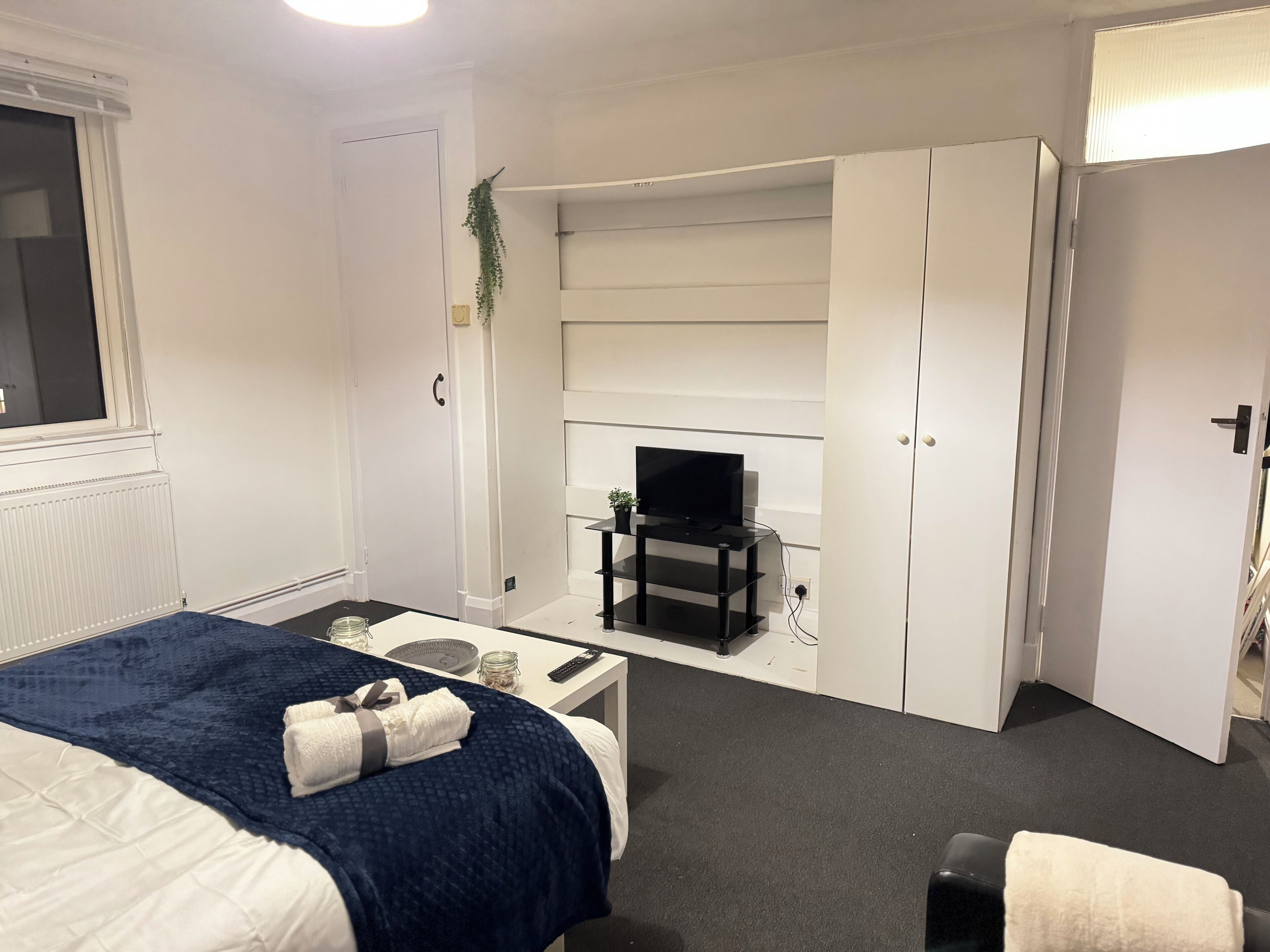Een hotelkamer met een bed, een bureau, een televisie op een standaard en een kledingkast.