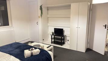 Een hotelkamer met een bed, een bureau, een televisie op een standaard en een kledingkast.