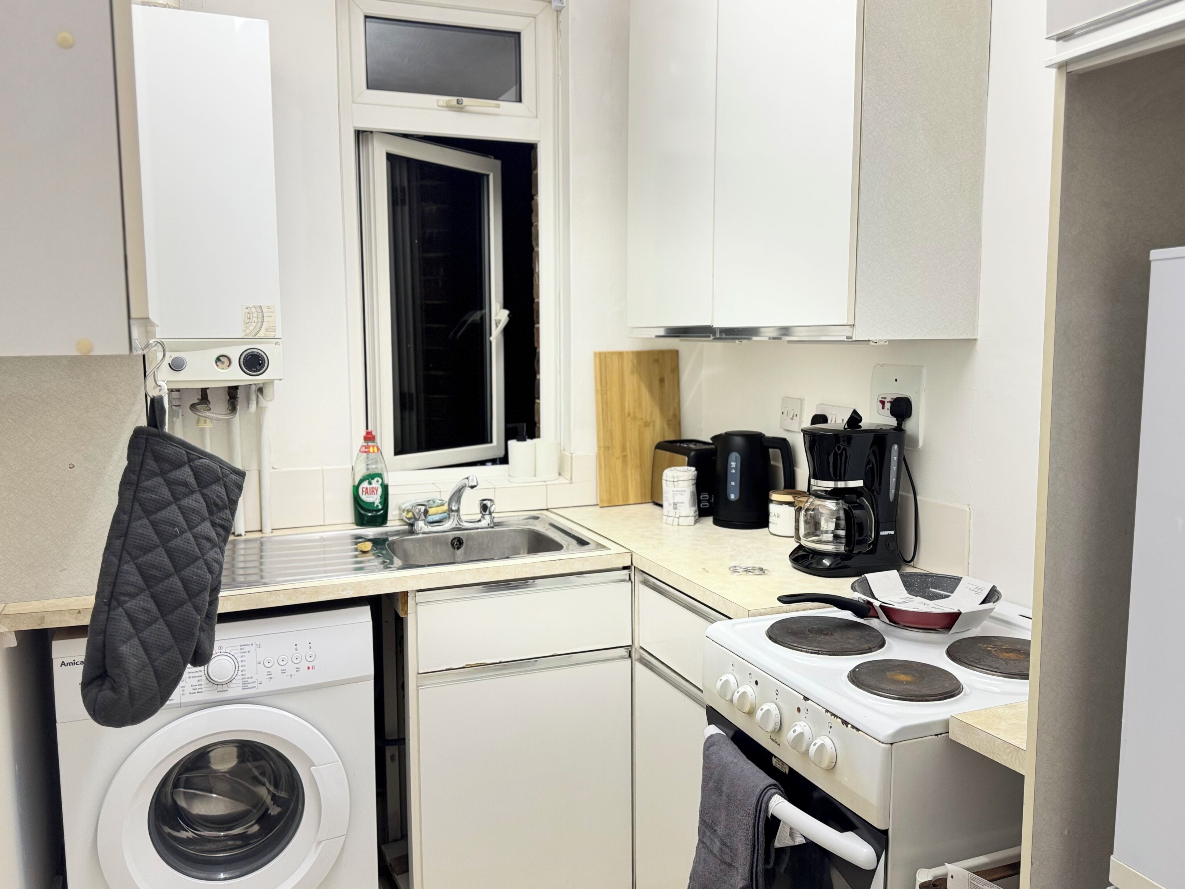 Una cucina compatta con lavatrice, fornello, macchina del caffè e una finestra.