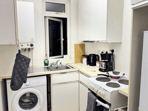 Cocina compacta con lavadora, estufa, cafetera y ventana.