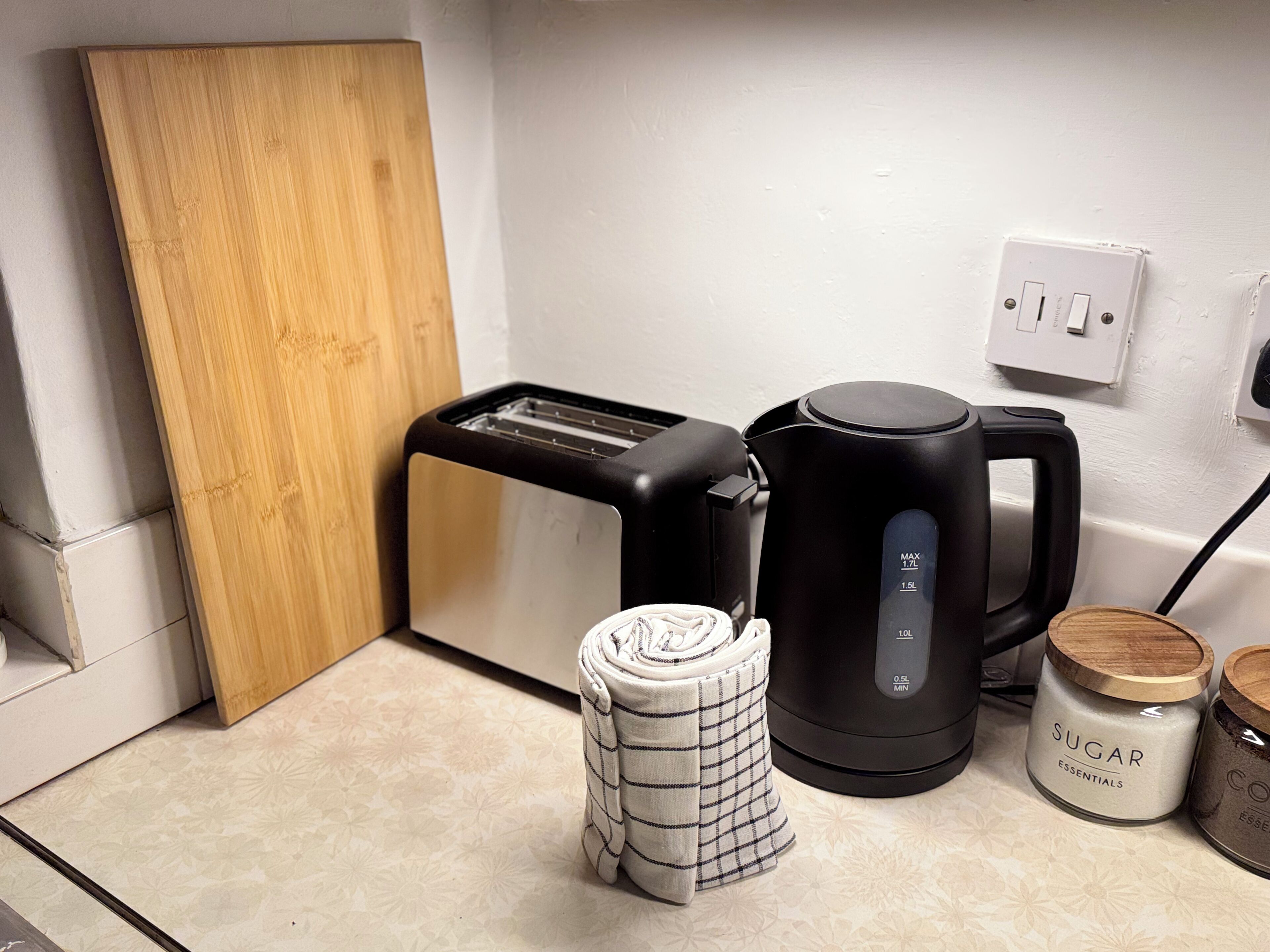Eine Küchenarbeitsplatte mit einem Toaster, einer Kaffeemaschine, einem aufgerollten Handtuch und Vorratseinkelchen mit der Aufschrift 'Zucker Basics'.