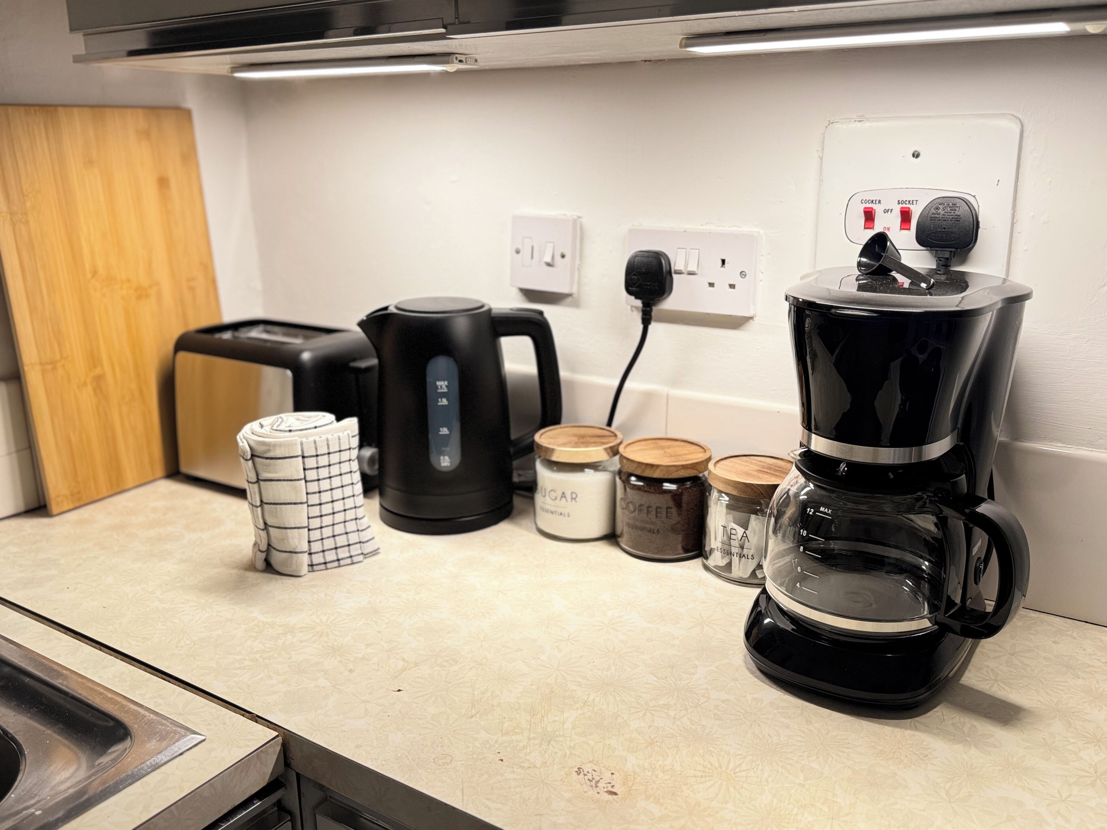 Eine Küchenarbeitsplatte mit Kaffeemaschine, Wasserkocher und Gläsern voller Tee und Kaffee.