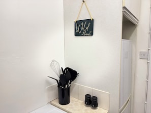 Eine Küchenzeile mit einem schwarzen Schild mit der Aufschrift 'Wild at heart' an der Wand, einem schwarzen Utensilienhalter mit einem Schneebesen und zwei Salzstreuern mit den Aufschriften 'P' und 'S'.
