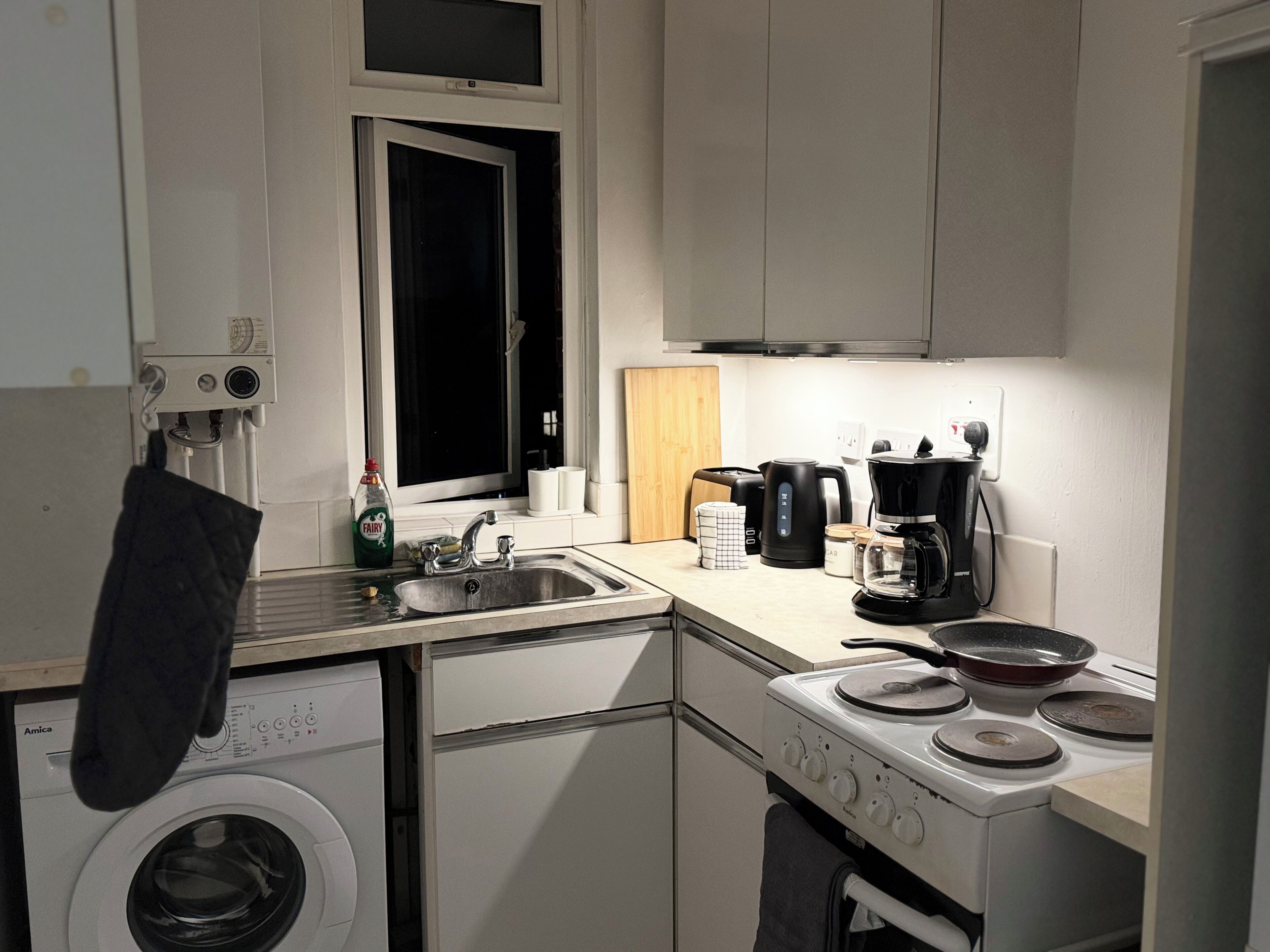 Een praktische keuken met een wasmachine, koffiezetapparaat en fornuis.