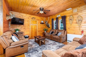 Ein Blockhaus-Interieur mit Kamin, Ledersofas, einem Fernseher und aufgehängten Hirschköpfen.