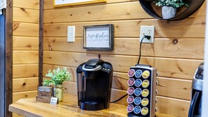 Eine Kaffeemaschine und eine Kapselmaschine auf einer Holzauslage mit einem Schild mit dem Aufdruck 'rise & shine' und einer kleinen Pflanze.