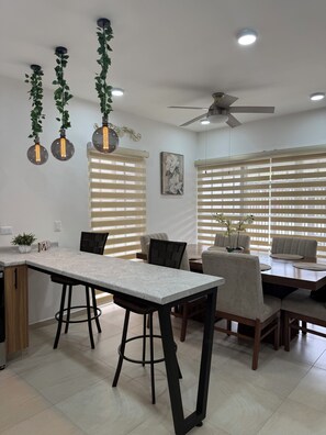 A modern kitchen with a marble countertop, bar stools, and pendant lighting with plants.
