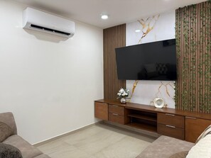 A modern living room with a flat-screen TV mounted on a wall with a marble-like design, a wooden entertainment unit below, and an air conditioning unit on the wall.