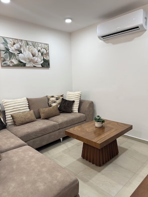 A modern living room with a beige sectional sofa, a wooden coffee table, and a large floral painting on the wall. - Casa Victoria | 3-Bedroom, 2.5 Baths, AC & Garage in City. Valleys (Ciudad Valles)