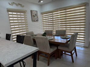 A dining area with a marble table, six chairs, and a large window with blinds. - Casa Victoria | 3-Bedroom, 2.5 Baths, AC & Garage in City. Valleys (Ciudad Valles)