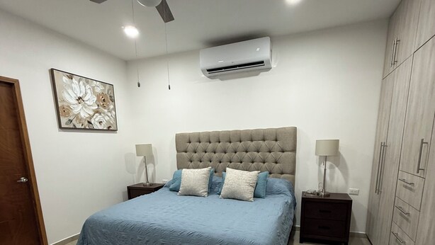 Ein Schlafzimmer mit einem Bett, Nachttischen, einem Deckenventilator, einer Klimaanlage und einem Kleiderschrank.