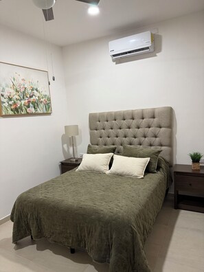 Ein Schlafzimmer mit einem großen Bett, einer Wand-Klimaanlage, einem Gemälde und einer Nachttischlampe.