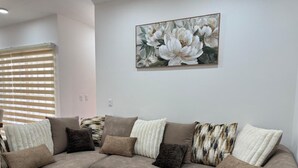 Ein beiges Ecksofa mit verschiedenen Kissen in unterschiedlichen Texturen und einem großen floralen Gemälde an der Wand.