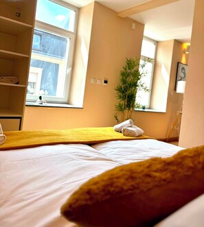 Quarto de hotel com uma cama, cabeceira amarela, janela e planta.
