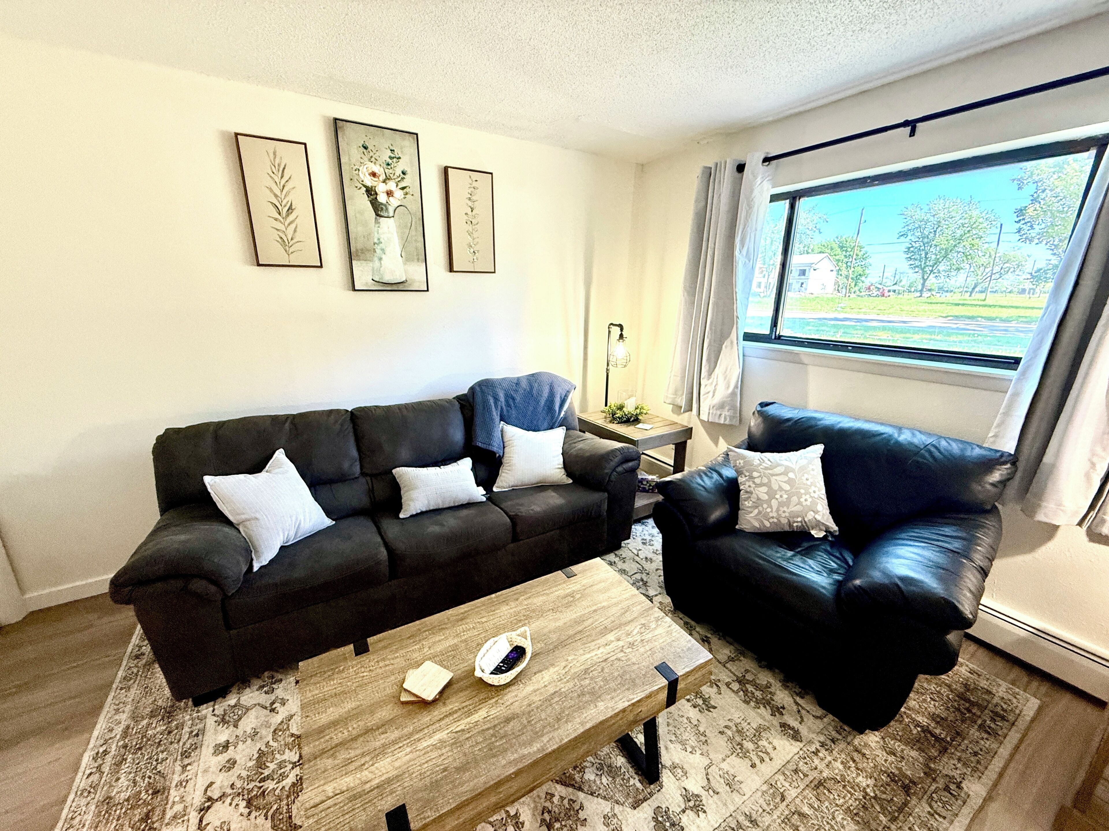 A living room with a dark brown sofa, a wooden coffee table, and a window with curtains.
