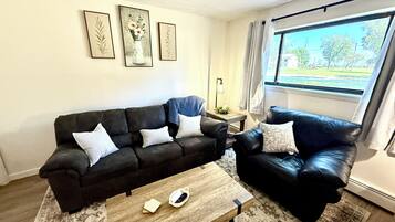 A living room with a dark brown sofa, a wooden coffee table, and a window with curtains.