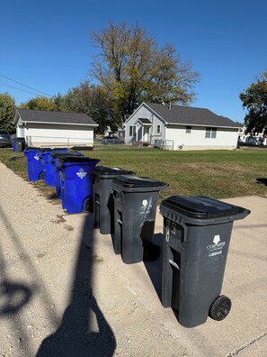 A row of black and blue garbage bins lined up on a concrete surface with houses in the background.