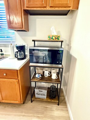 A kitchen with wooden cabinets, a microwave on a metal shelf, a coffee maker, and a basket labeled 'Recycle'.