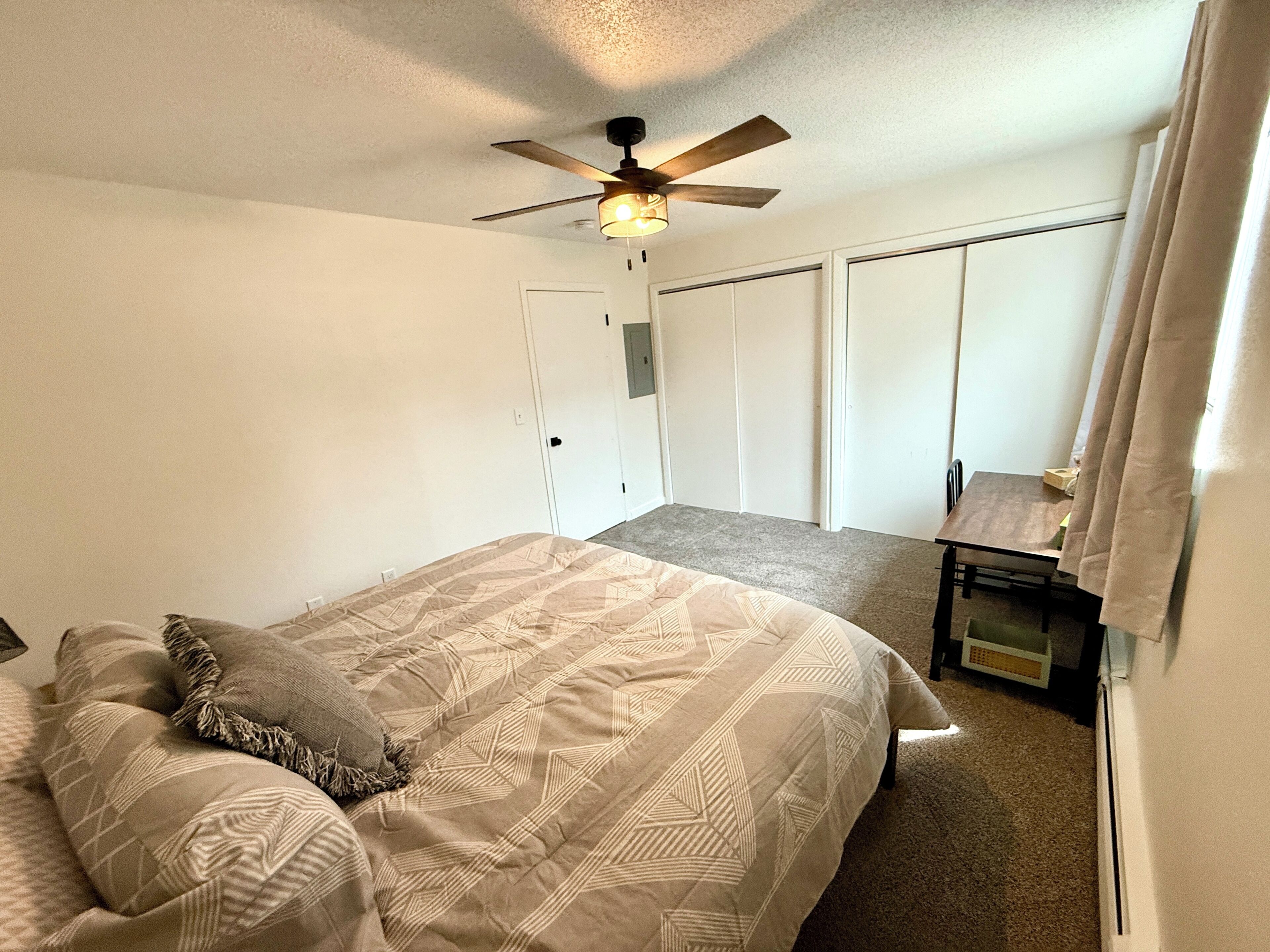 Une chambre à coucher comprenant un lit, un ventilateur de plafond, un bureau et une armoire.