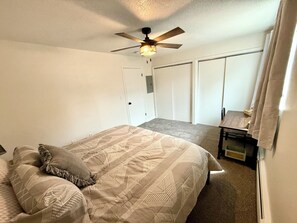 A bedroom with a bed, a ceiling fan, a desk, and a wardrobe.