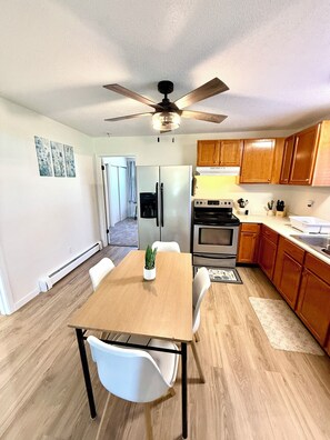 A modern kitchen with wooden cabinets, a central island, a ceiling fan, and a refrigerator.