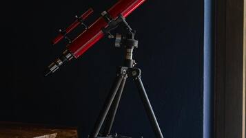 A telescope on a tripod in a room with a dark wall and a window.