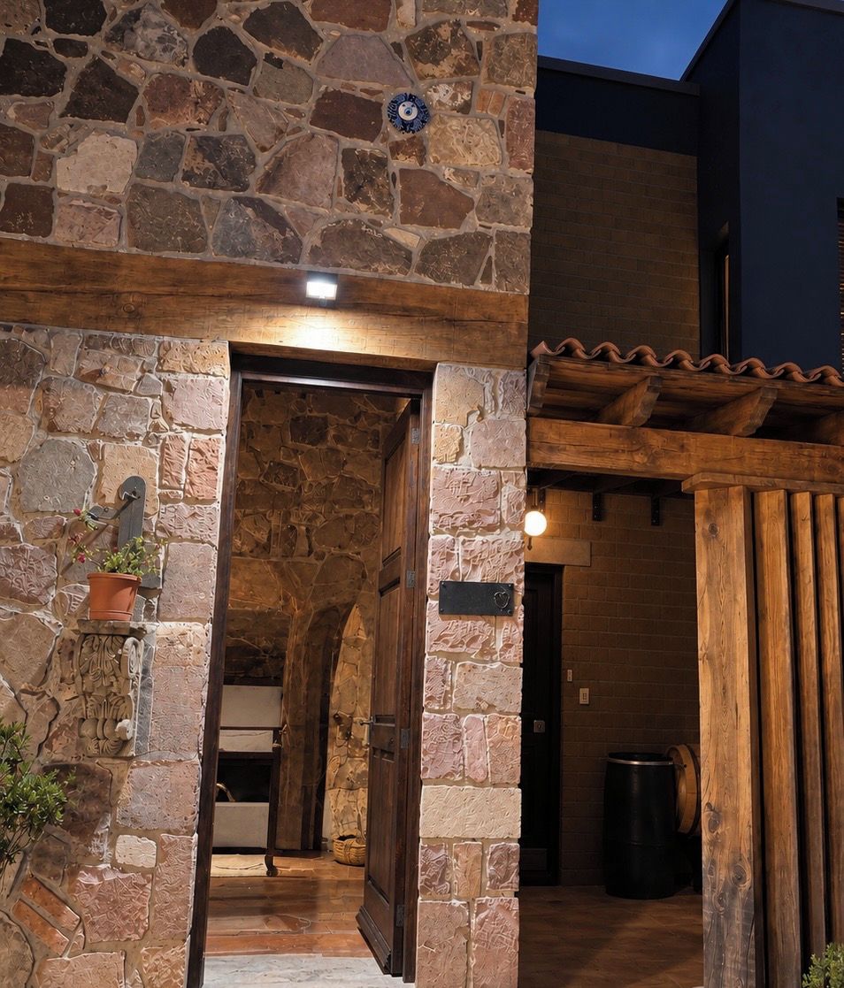 Entrada de un edificio de piedra con una puerta de madera, una planta en maceta y un letrero de metal.