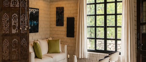 A room with a white sofa, a wooden cabinet, a patterned rug, and a large window with curtains.