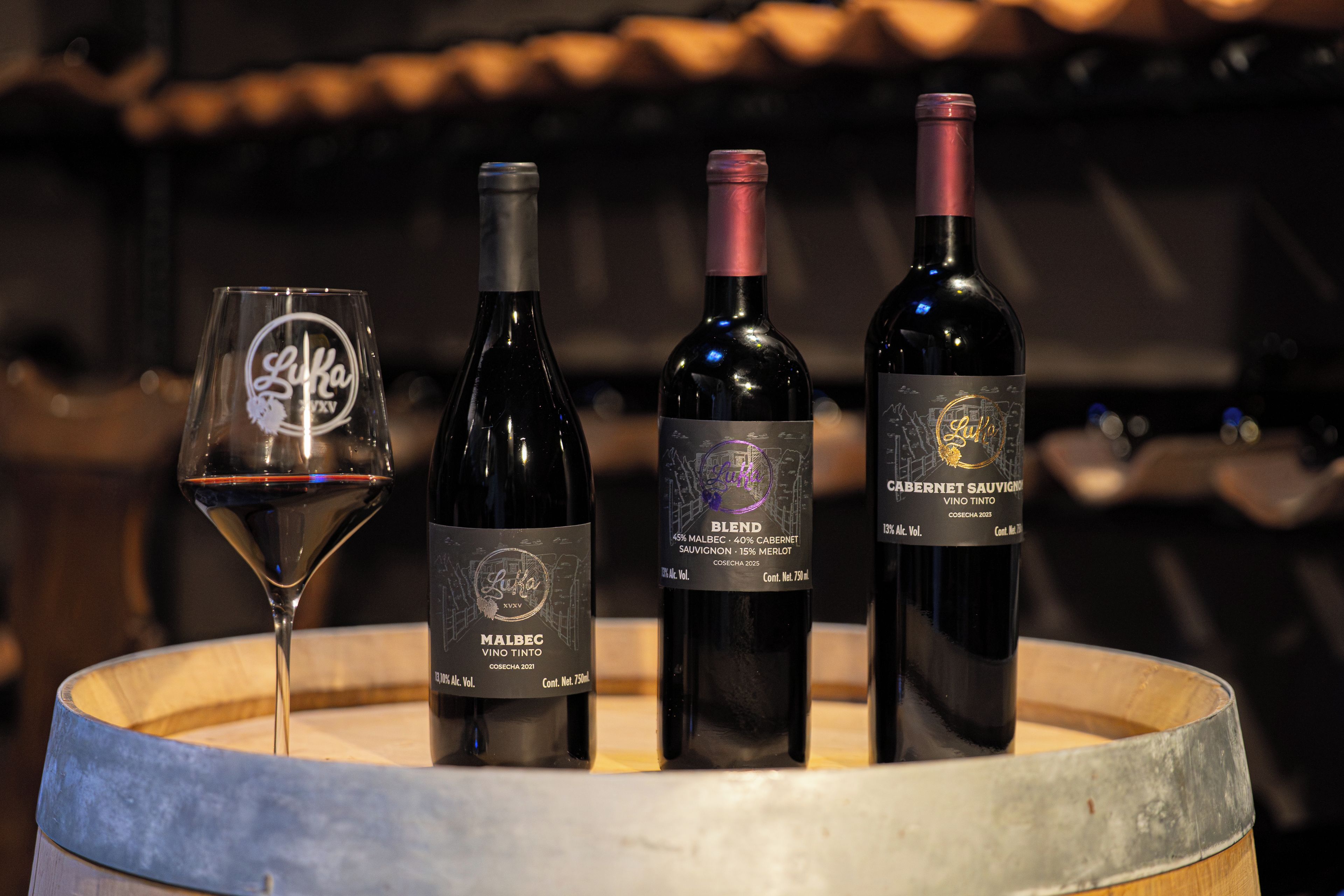 Three wine bottles and a wine glass on a wooden barrel.