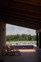 Un espacio de estar al aire libre cubierto con dos sillones, vista a un jardín ajardinado y una pared de ladrillo.