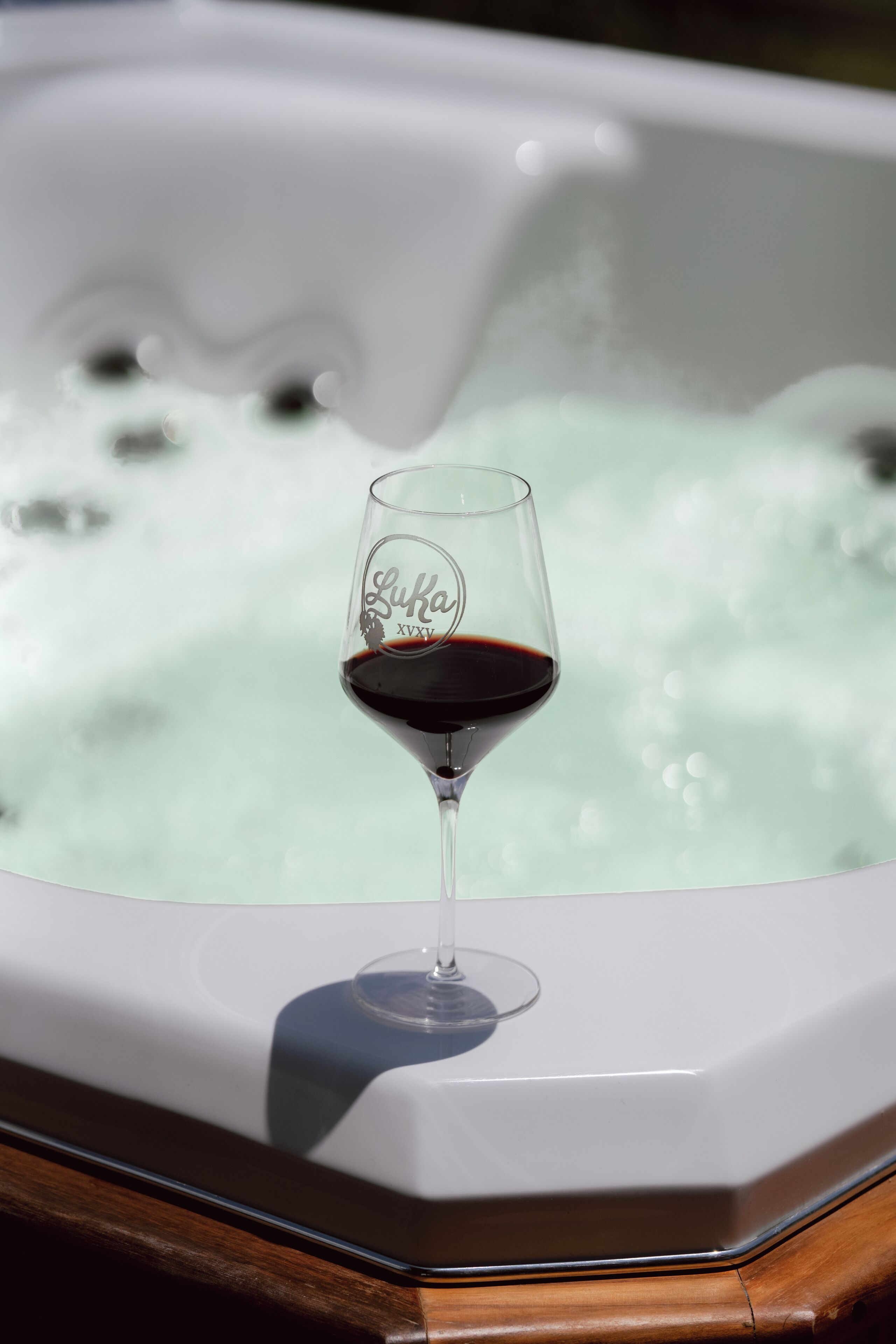 Un verre de vin rouge posé sur une surface en bois, avec un jacuzzi en arrière-plan.