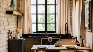 Ein Essbereich mit Backsteinwand, Holzbalken, einem fenster mit Vorhängen, einem Tisch für zwei Personen und einem Kühlschrank.